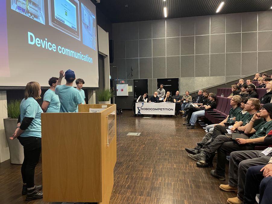 Foto: Kuben 2026 Team 1 w audience en person som holder en presentasjon for en gruppe mennesker