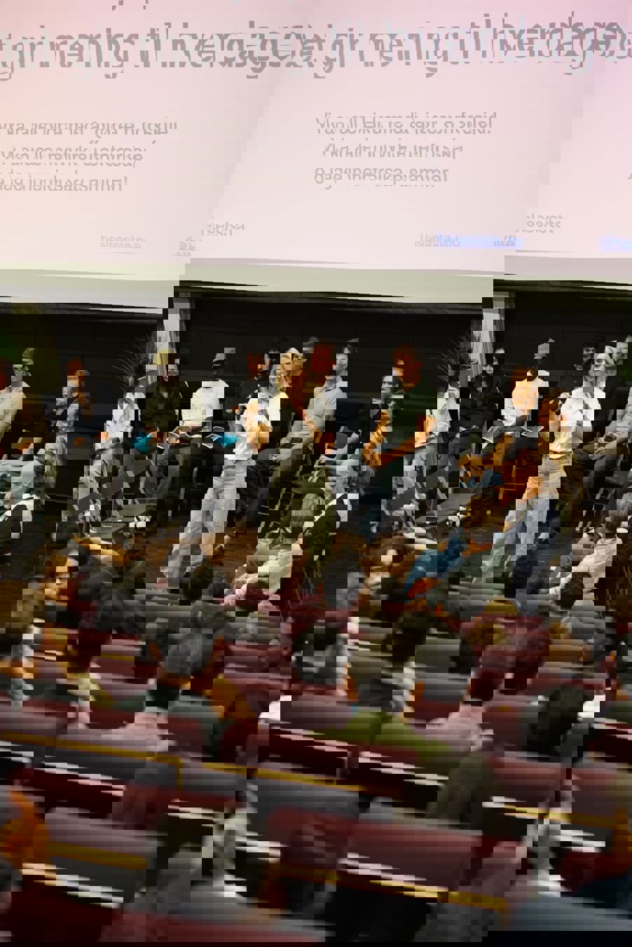 en person som står foran en gruppe mennesker som sitter i stoler